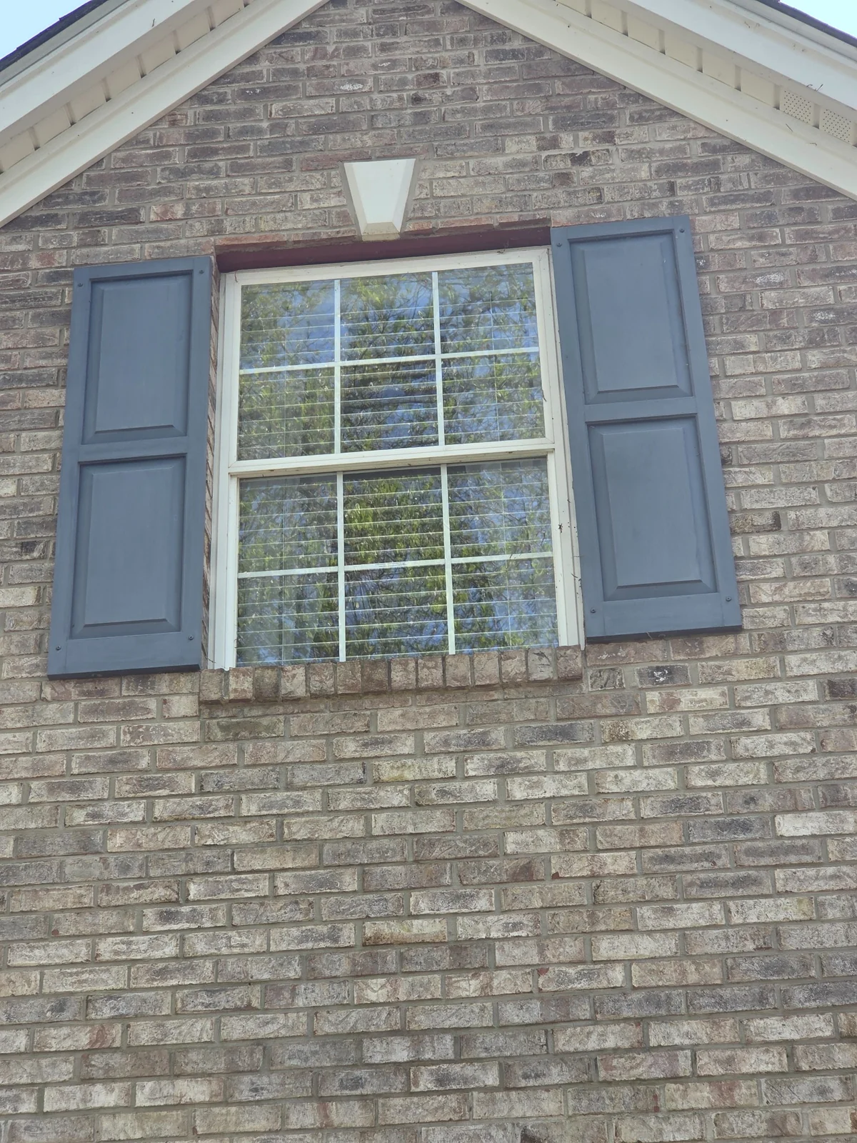 Exterior shutters beside a window on a brick home